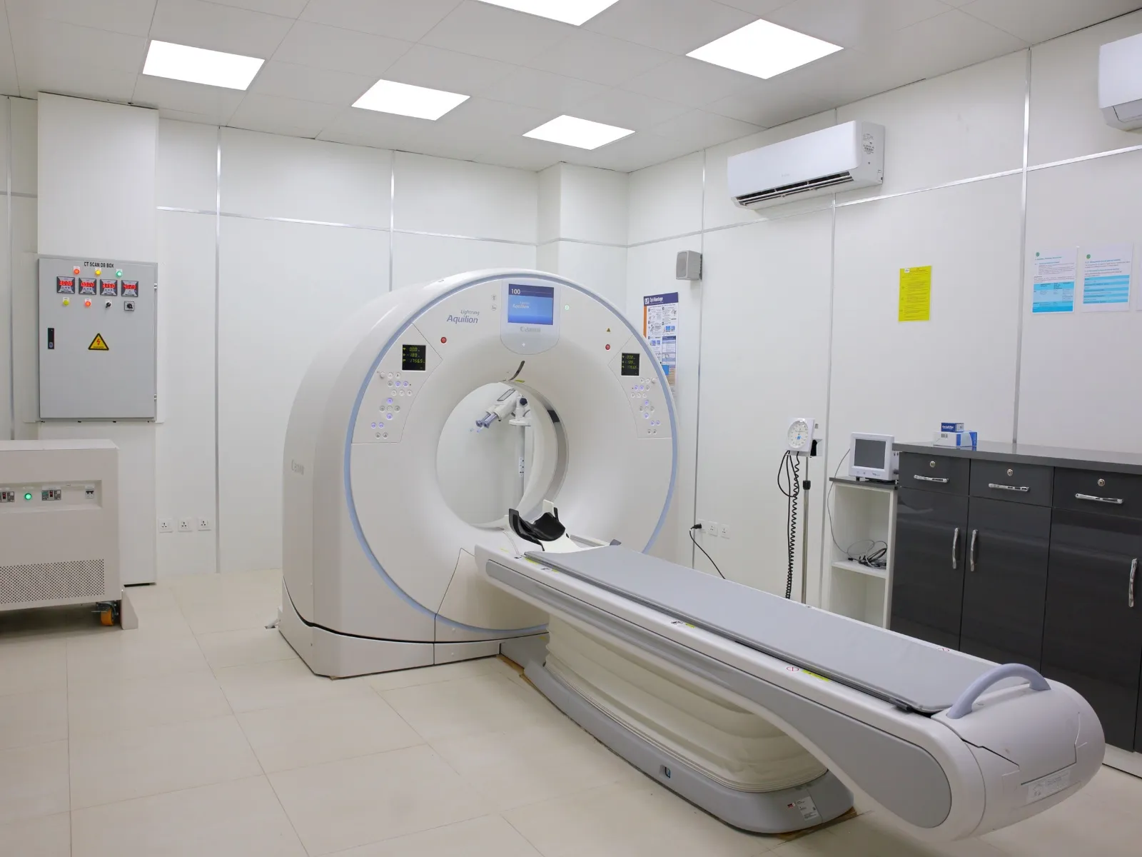 Una sala per la tomografia computerizzata: lo scanner bianco con il lettino, armadi scuri e pareti chiare sotto le plafoniere.